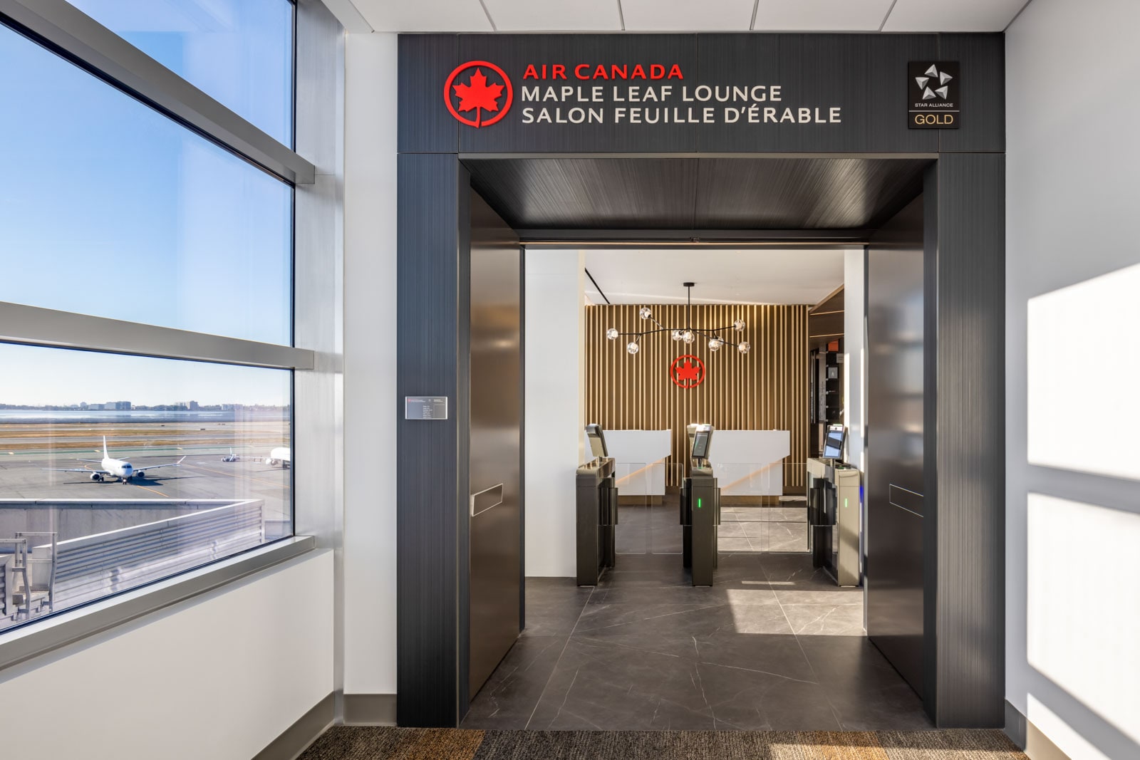 A windowed hallway leads to the entrance of the Maple Leaf Lounge at San Francisco Airport.